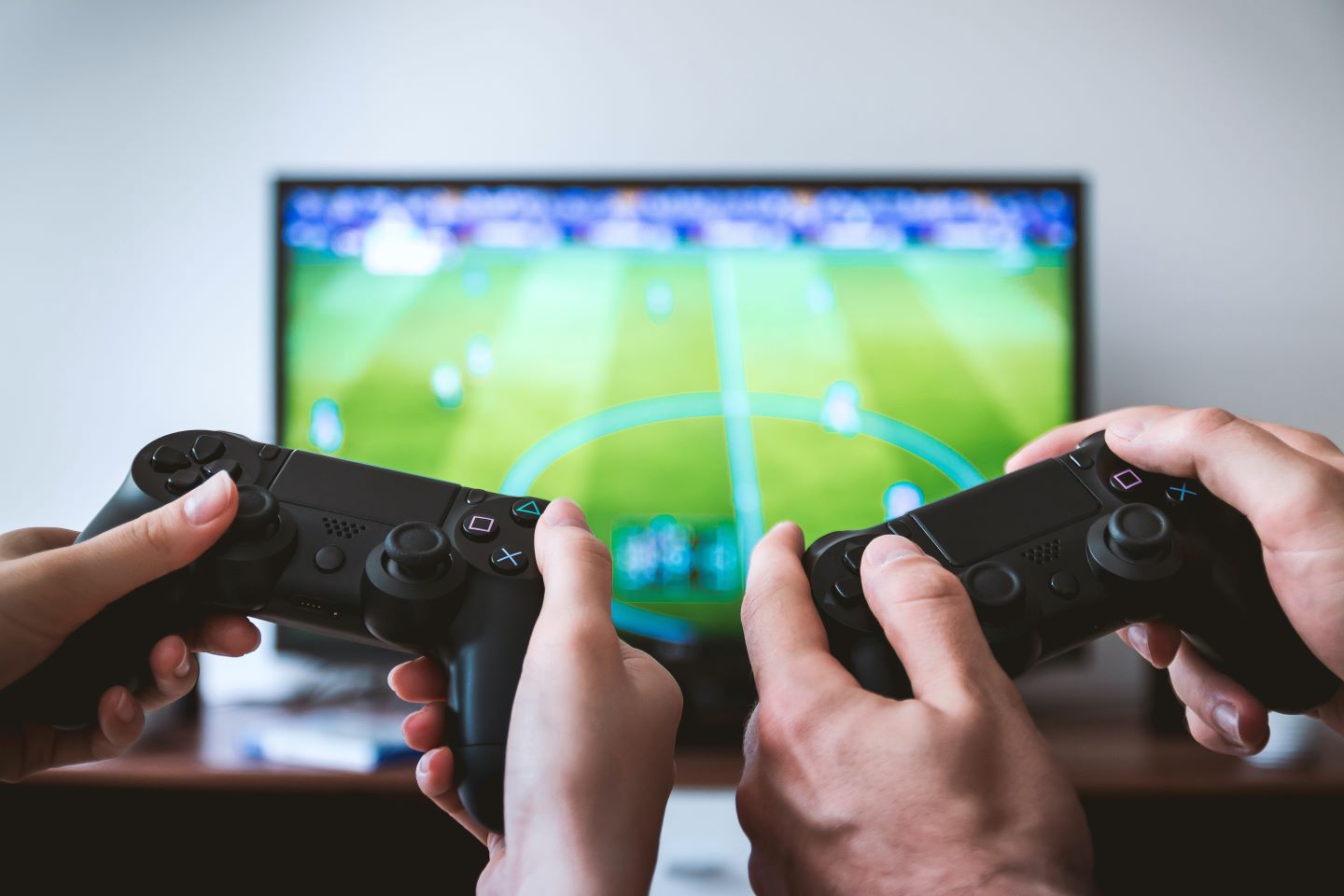 Mãos de duas pessoas segurando o controle de vídeo game em um jogo de futebol