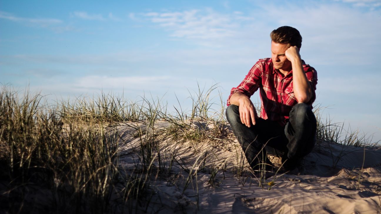 homem sentado na areia com grama pensando