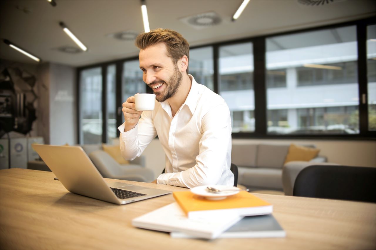 Homem trabalhando no computador e tomando café representando o post sobre empregos para quem fala inglês